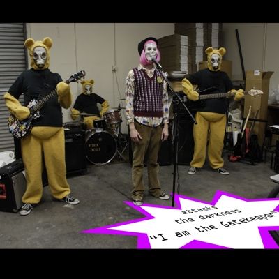 Warehouse with a band playing where the singer has a skull mask and ugly sweater on and the rest of the band is yellow bears with black shirts and gas masks on